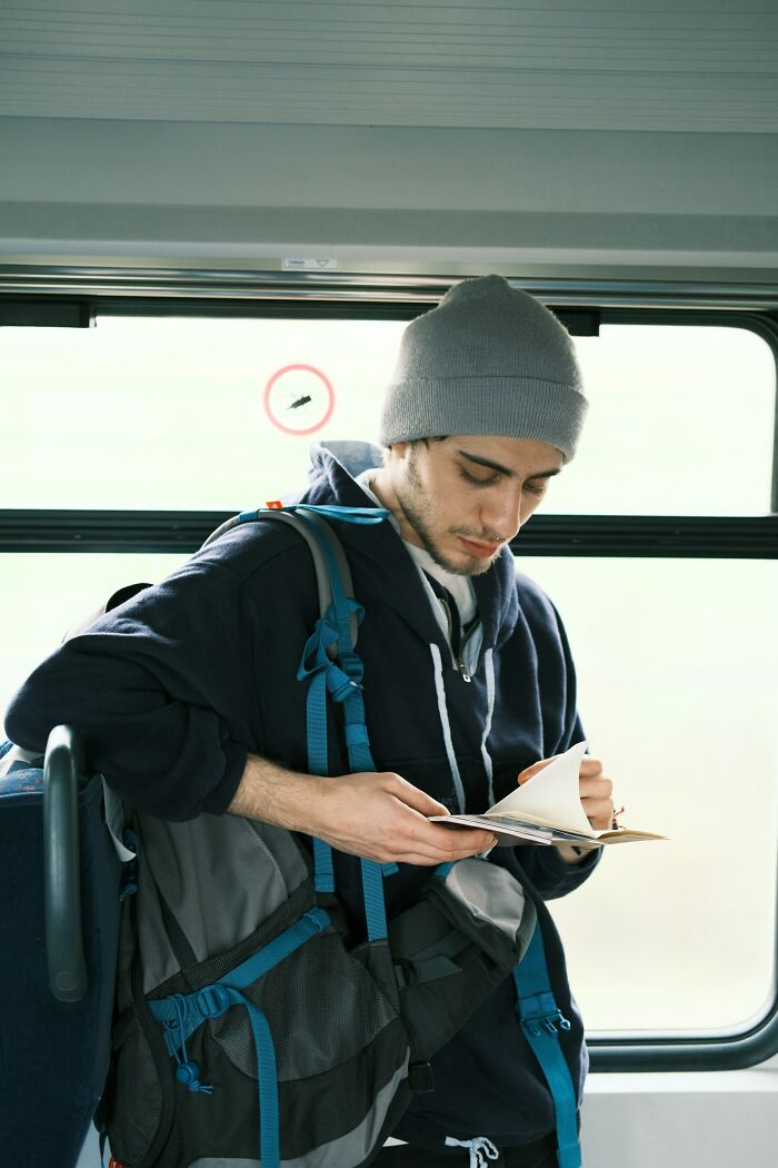 Young man in a beanie on a bus reading a notebook, capturing a moment related to close friend realization jerk stories.