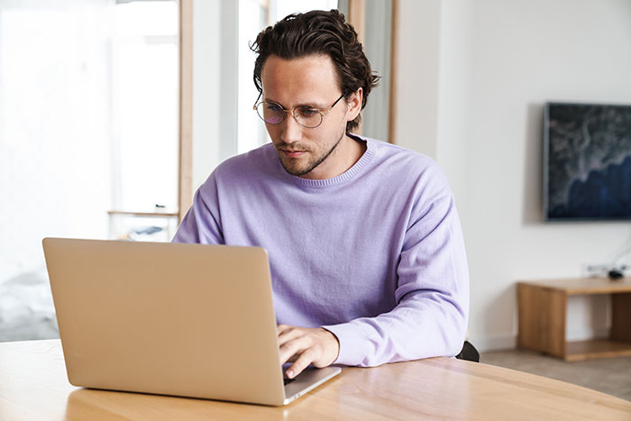 Man in glasses and purple sweater focused on laptop, representing non-profit employee accused of fudging hours.