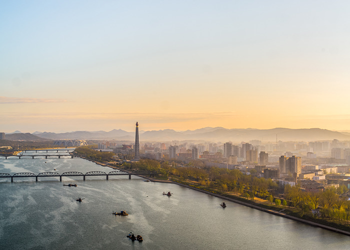 Aerial view of a North Korean city at sunset with bridges and river, highlighting smuggled smartphone control measures.