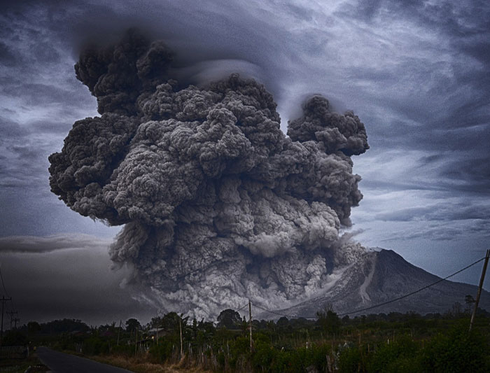 Volcanic eruption with massive smoke cloud under dark swirling skies, illustrating cosmic chaos and Nostradamus predictions.