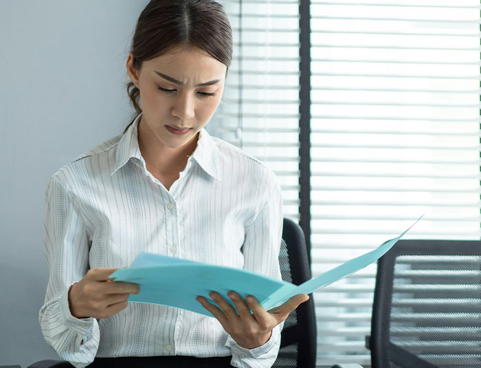 Young woman in office reviewing legal documents with a confused expression, relating to absurd legal claims discussion.
