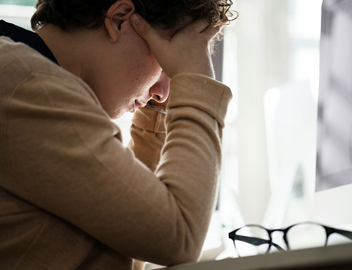 Young person stressed with head in hands, sitting by a computer, illustrating absurd legal claims frustration.