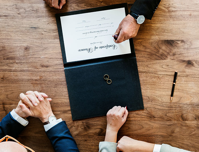 Couple at a table with marriage certificate and two rings, illustrating absurd legal claims concept.