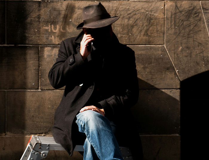 Man in a dark coat and hat sitting against a wall, possibly making absurd legal claims or discussing lawyer matters.