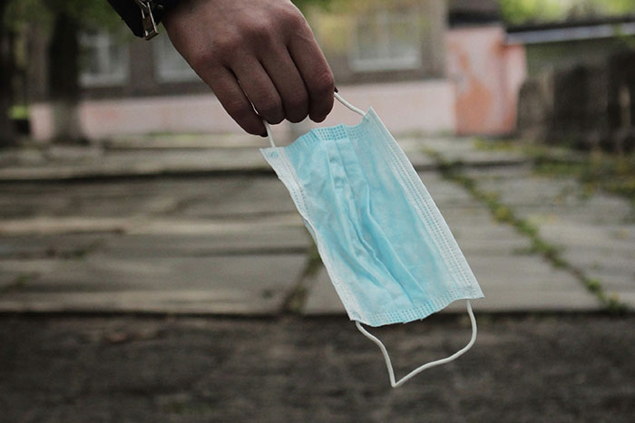 Hand holding a disposable face mask outdoors symbolizing challenges faced by healthcare workers during critical moments.