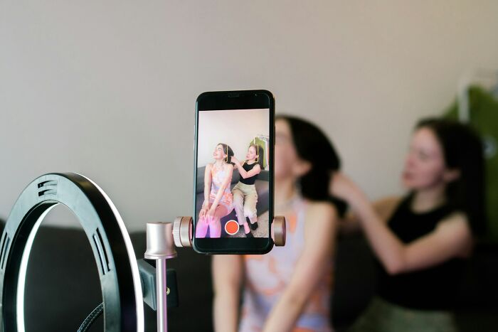 Two women recording a video on a smartphone with ring light, sharing opinions on current situation and social topics.