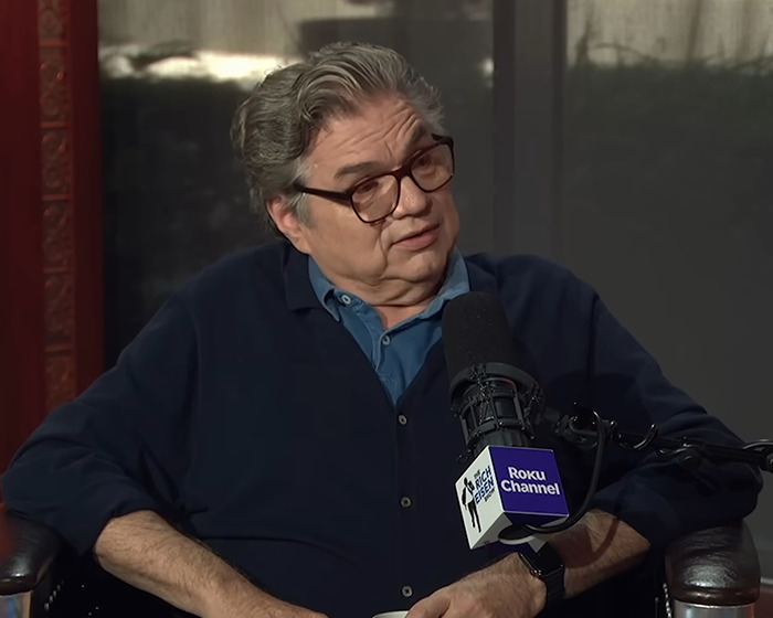 90s actor with glasses in a dark blue shirt speaking into a Roku Channel microphone during an interview session. 90s actor with glasses in a dark blue shirt speaking into a Roku Channel microphone during an interview session.