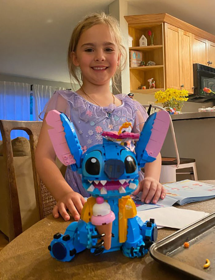 Young girl smiling behind colorful toy on table, related to bodies of 3 missing sisters found, police hunt for father.