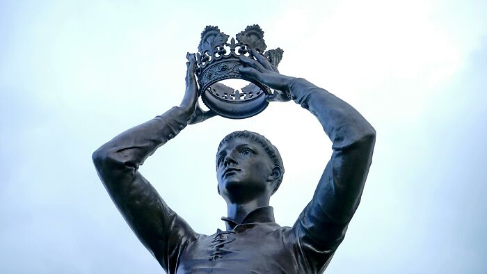 Statue of a man holding a crown above his head against a cloudy sky, representing one Mississippi counting countries.