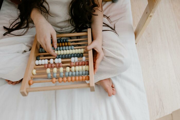 Child counting colorful beads on an abacus while sitting on a white bed, representing one Mississippi counting countries concept.