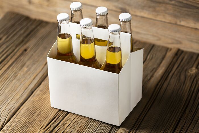 Six glass bottles with golden liquid in a white carrier box on wooden surface, illustrating one Mississippi counting countries.