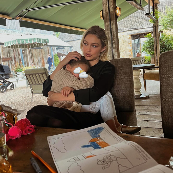 Gigi Hadid holding daughter Khai at a rustic outdoor cafe with a child’s drawing on the table nearby. Gigi Hadid holding daughter Khai at a rustic outdoor cafe with a child’s drawing on the table nearby.