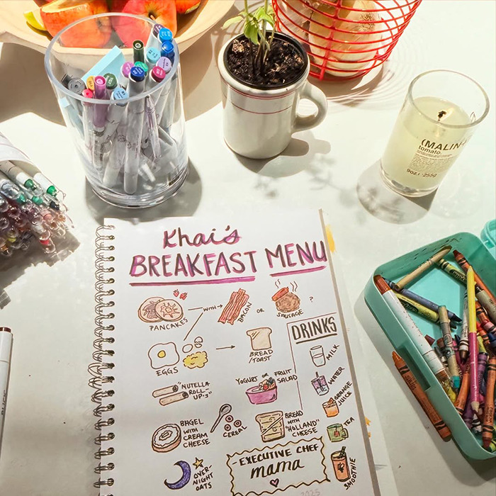 Hand-drawn breakfast menu including pancakes, eggs, and drinks on a table with markers and crayons nearby. Hand-drawn breakfast menu including pancakes, eggs, and drinks on a table with markers and crayons nearby.