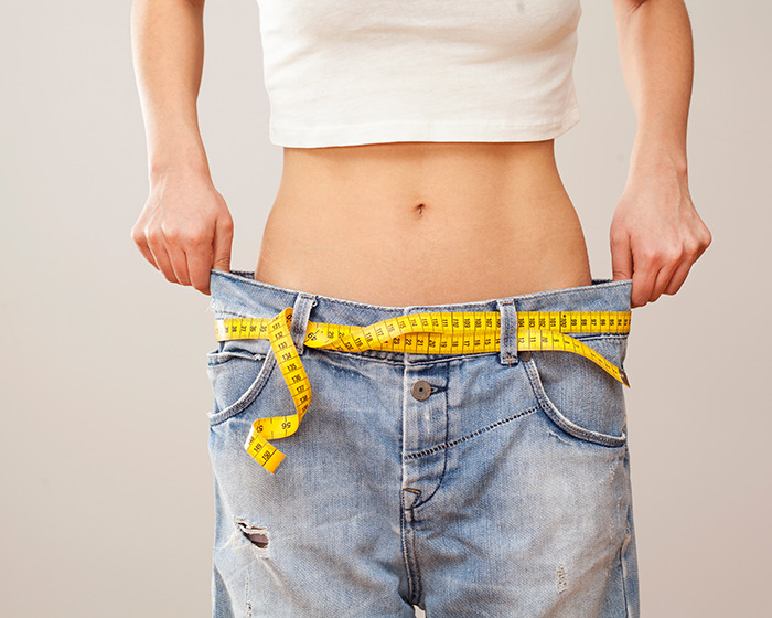 Person wearing oversized jeans with a yellow measuring tape around the waist symbolizing organ-destroying effects of Ozempic and Mounjaro.