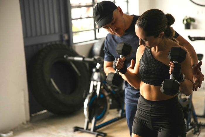 A personal trainer assisting a woman lifting dumbbells, highlighting people and unresolved personal mysteries.