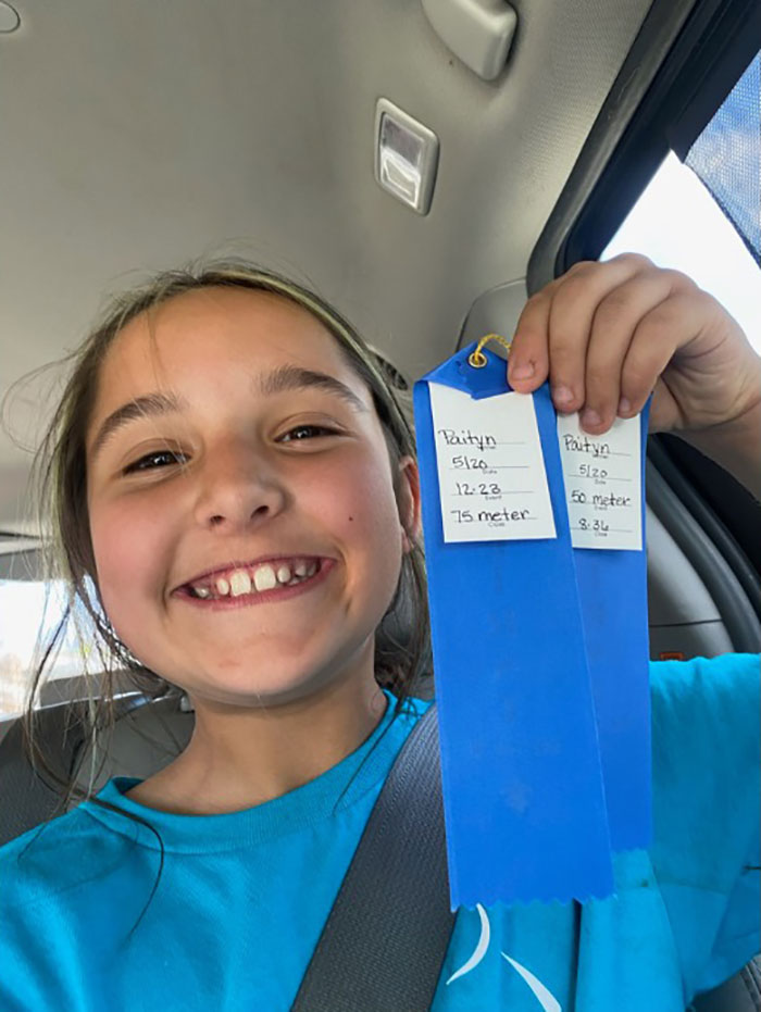 Smiling young girl holding blue ribbons inside a car, related to missing sisters case and police search for their father.