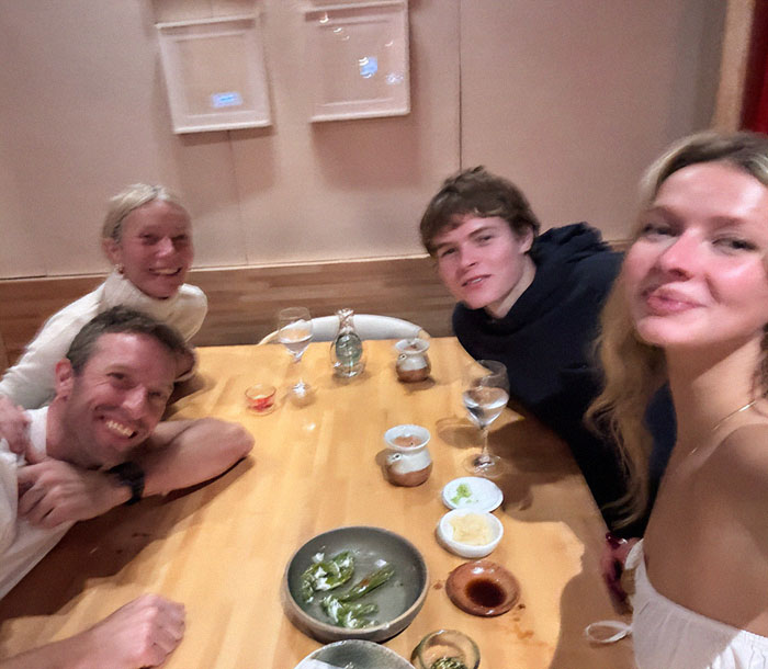 Apple Martin and family gathered around a dining table, with Gwyneth Paltrow and drinks, related to Apple Martin roasting mom post backlash. Apple Martin and family gathered around a dining table, with Gwyneth Paltrow and drinks, related to Apple Martin roasting mom post backlash.