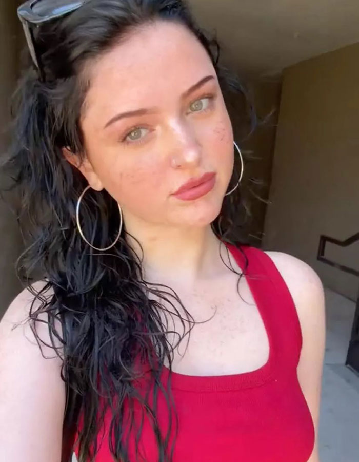 Young woman with long dark hair and hoop earrings in a red top, highlighting warning about dusting challenge dangers.