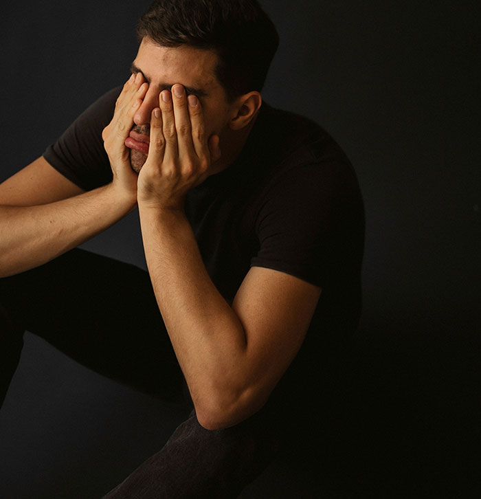 Man in black shirt sitting with hands covering face, reflecting the emotional impact of parents disowning their children.