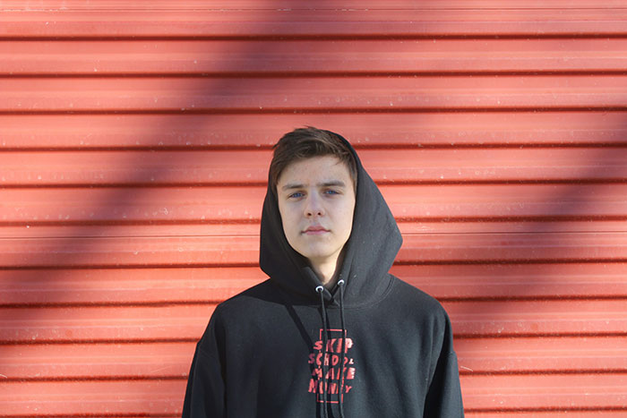 Teenage boy in black hoodie standing against a red wall, illustrating themes of parents who disowned their children.