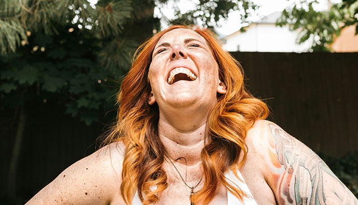 Red-haired woman outdoors laughing with tattooed arm visible, illustrating emotions tied to parents who disowned their children.