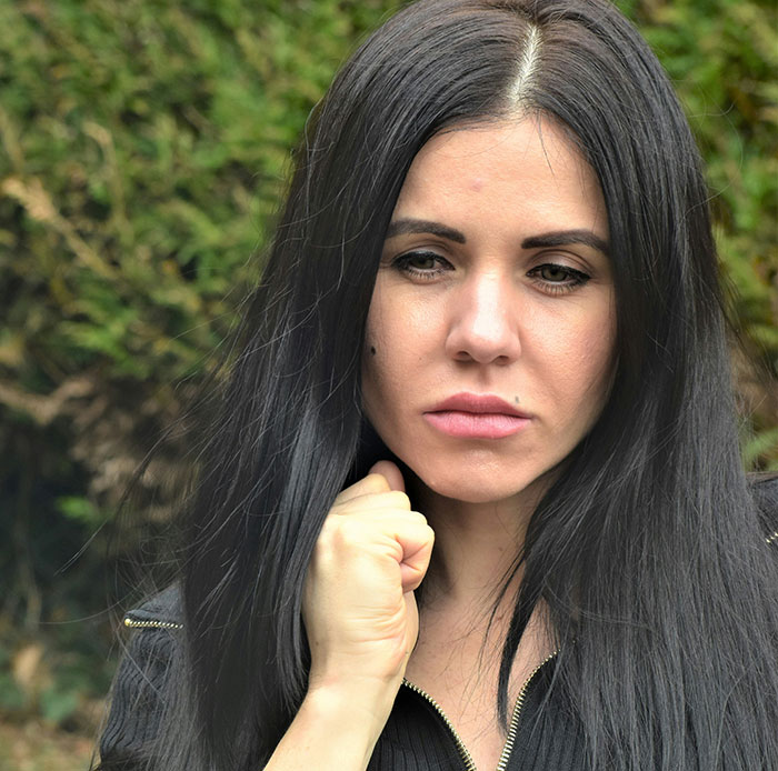 Sad woman outdoors with black hair and dark jacket, reflecting on difficult moments related to parents who disowned their children.