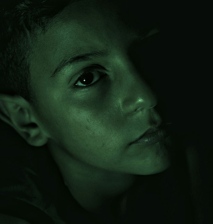 Close-up of a young person with a solemn expression in dark lighting, representing parents who disowned their children.