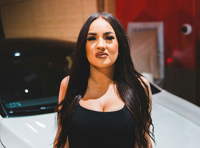 Woman with long dark hair standing in front of a car, reflecting on reasons parents disowned their children.