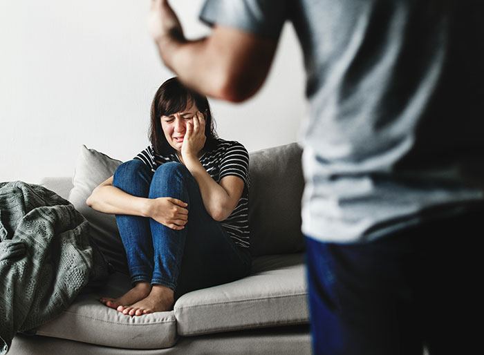 Woman sitting on a couch crying while a man stands nearby, representing parents who disowned their children.