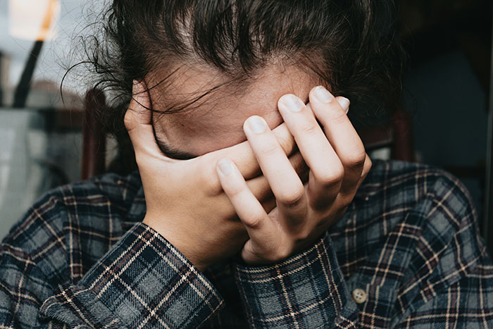 Person in plaid shirt covering their face with hands, representing emotional struggles related to parents disowning their children.