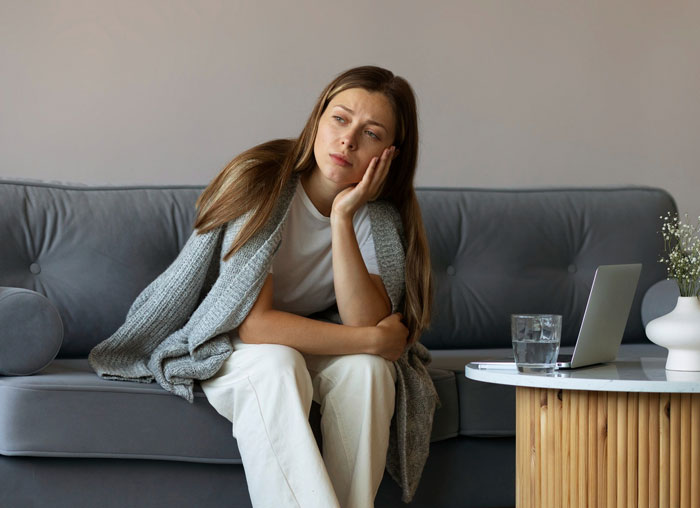 Young woman sitting on a couch looking upset, reflecting on damaged car, dishes, and furniture in relationship conflict scenario.