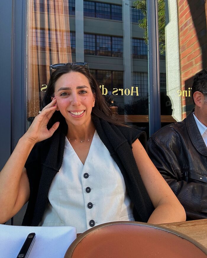 Woman smiling at outdoor cafe, casually dressed, illustrating plane passenger slammed after making salad mid-flight story. Woman smiling at outdoor cafe, casually dressed, illustrating plane passenger slammed after making salad mid-flight story.