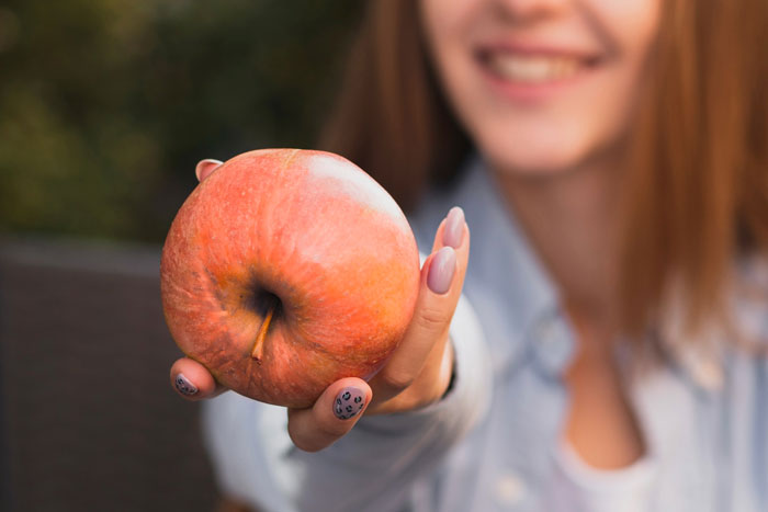A woman smiling and holding an apple related to K9 sniffing undeclared fruit in passenger luggage.