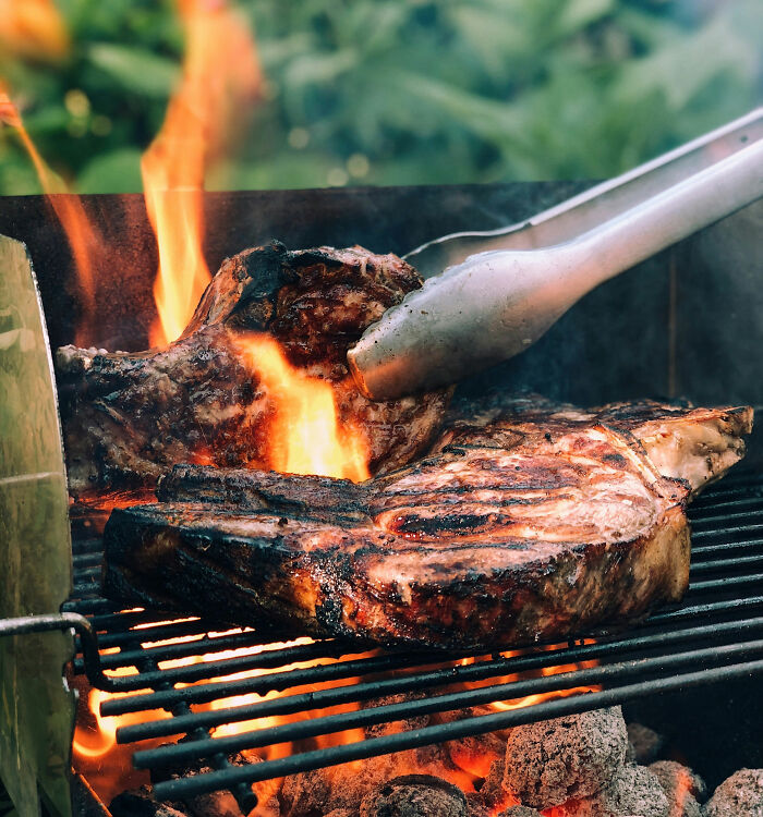 Grilled meat over open flame with tongs turning food, highlighting tobacco and health risks related to smoking.