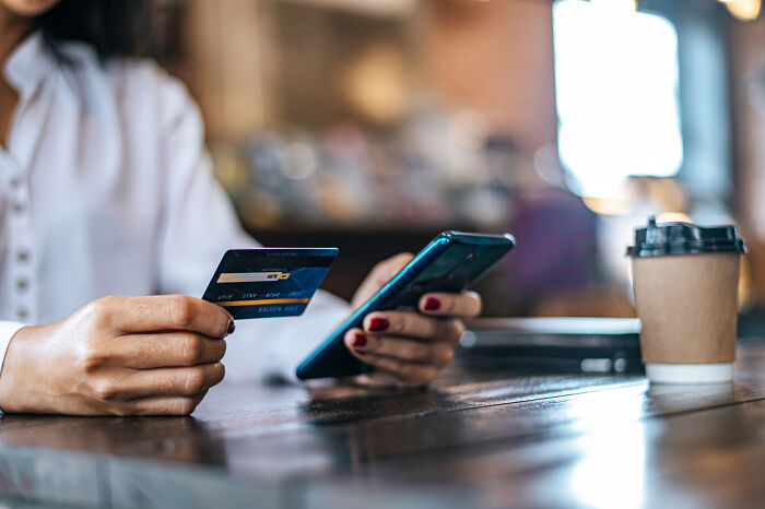 Person holding credit card and smartphone in a café.