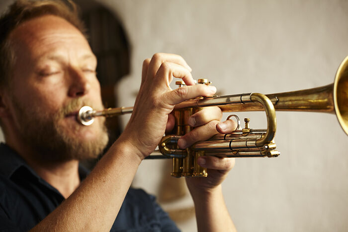 Man playing a trumpet indoors, illustrating skills people online needed before the 2000s but don’t need anymore.