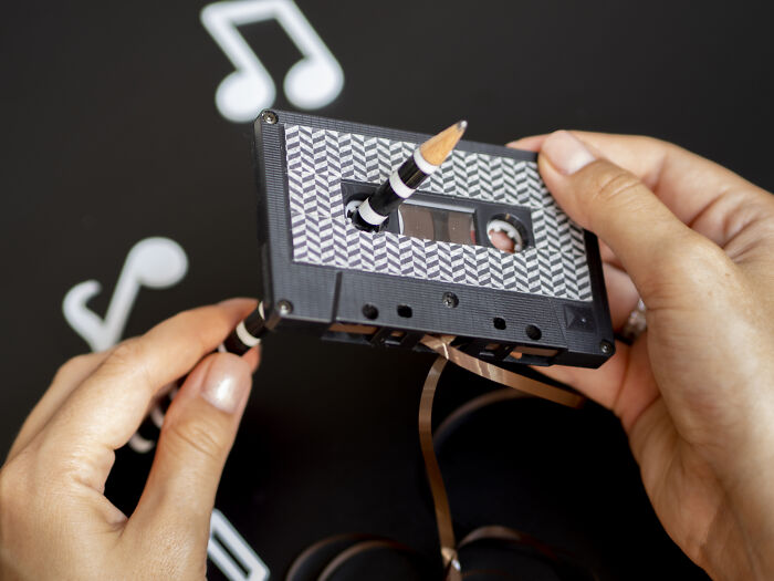 Hands using pencil to rewind audio cassette tape, illustrating skills people online needed before the 2000s but don't need now.