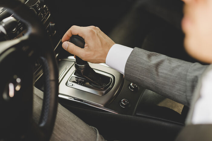 Person in a suit operating a car gear shift, illustrating skills people online needed before the 2000s but not anymore.