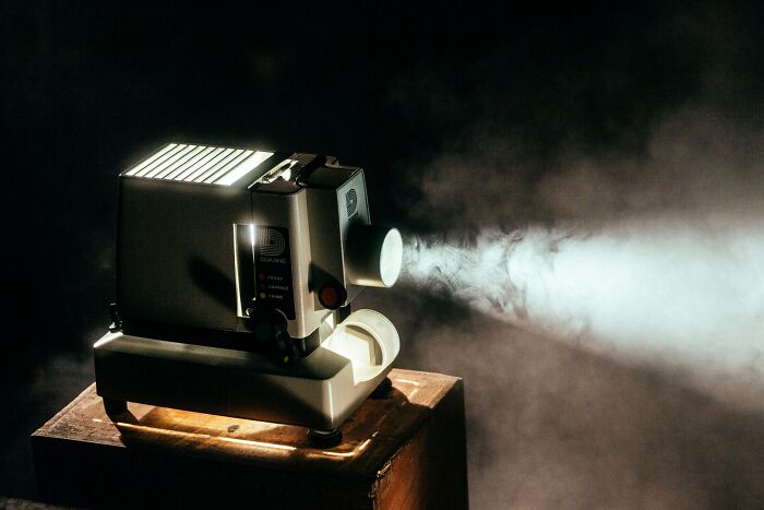 Vintage film projector casting light beam in dark room representing skills people online needed before the 2000s.