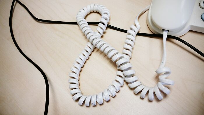 Coiled landline phone cord on a wooden desk representing skills people online needed before the 2000s.