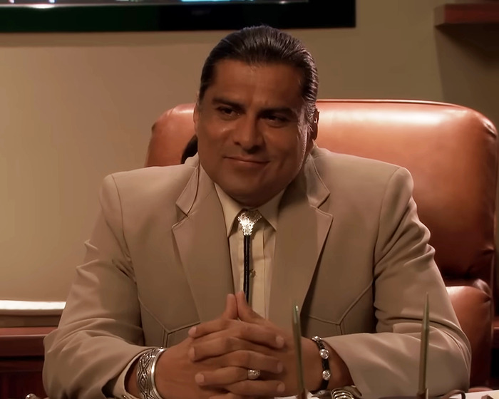 Man in beige suit sitting at desk, linked to discussions about Chris Pratt and Parks And Rec co-star tribute controversy.