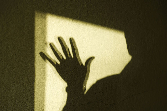 Shadow of a raised hand on a wall symbolizing the frightening experiences of people who experienced psychosis.