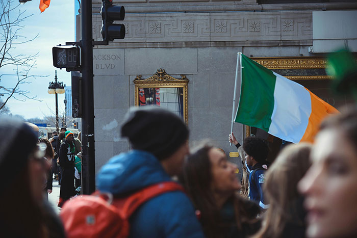 Crowd gathering outdoors near a building with someone holding a green, white, and orange flag, illustrating psychosis experiences.