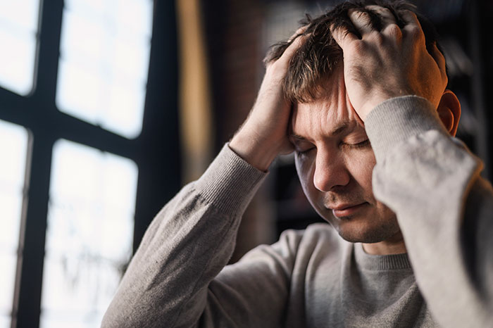 Man in gray sweater holding head in hands, appearing distressed, reflecting experiences of psychosis and terrifying feelings.