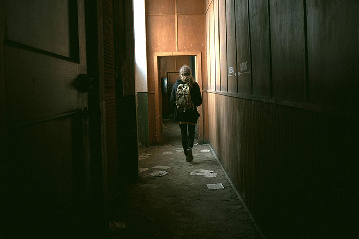 Person walking alone in a dimly lit narrow hallway, evoking a sense of fear linked to psychosis experiences.