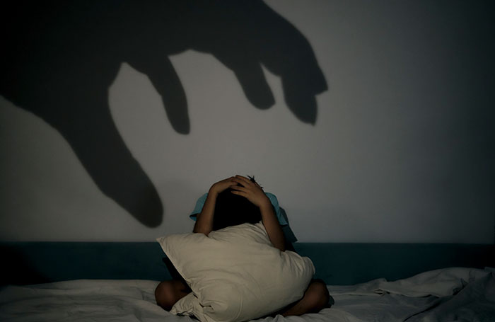 Person holding a pillow on bed, shadow of a large hand looming, depicting terrifying psychosis experiences.