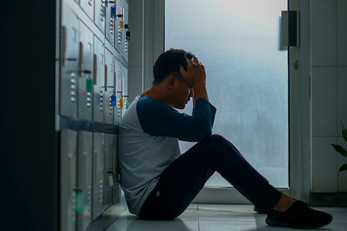 Person sitting on the floor by lockers holding their head, depicting distress from psychosis and terrifying feelings.