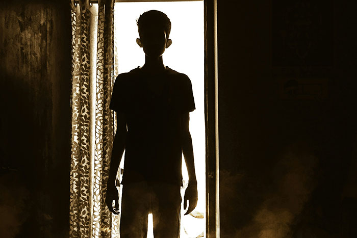 Silhouetted person standing in a dim room with light from a doorway, representing psychosis and terrifying visions.