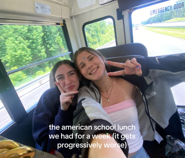 Two teens smiling on a bus showing reactions to American school lunches described as progressively worse over a week