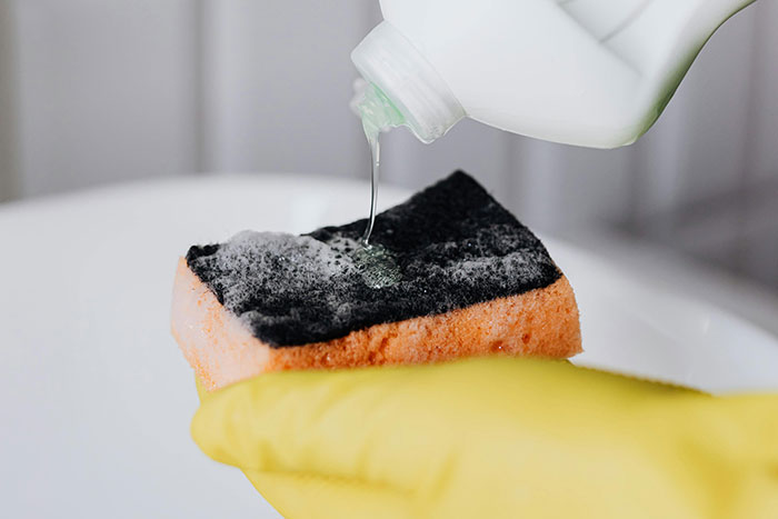 Close-up of a hand in yellow glove pouring cleaner on a sponge, illustrating times people said something so stupid.